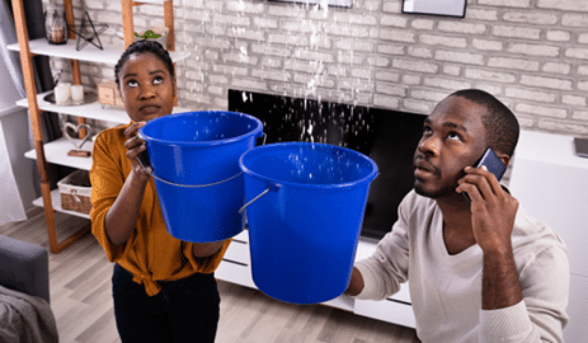 Couple on the phone holding buckets catching water drips from the ceiling